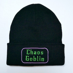 May include: Black knit beanie with a purple and green embroidered patch that says "Chaos Goblin".