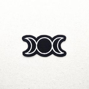 May include: Black and white embroidered patch featuring the Triple Moon symbol. The design consists of a central circle with two crescent moons on either side. The patch has a black background with white stitching.