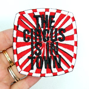 May include: Red and white striped iron-on patch with the text "The Circus is in Town" in black.