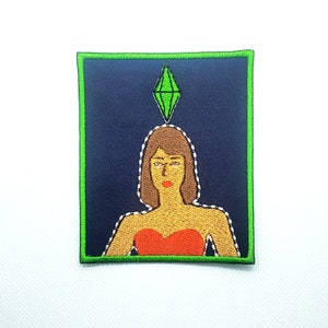 Peut inclure: Patch en forme de diamant vert avec une femme en robe rouge et cheveux bruns. Le patch a une bordure verte.