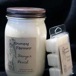 May include: A glass jar candle with a brown lid and a label that reads "The Grumpy Farmer Georgia Peach". The candle is hand-poured soy wax and is not for human consumption. A small package of wax melts is also shown in the image.