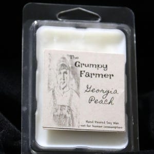May include: A white soy wax melt in a clear plastic container with a label that reads "The Grumpy Farmer Georgia Peach" and "Hand Poured Soy Wax - not for human consumption."