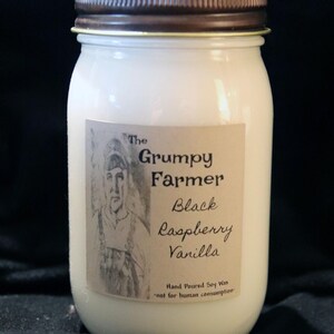 May include: A white glass jar candle with a brown lid. The label reads "The Grumpy Farmer" and "Black Raspberry Vanilla". The label also states "Hand Poured Soy Wax" and "not for human consumption".