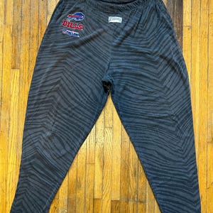May include: Gray sweatpants with a zebra print pattern. The sweatpants have a black and blue Buffalo Bills logo with the text "Bills" and "NFL" on the left leg.