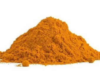 May include: A conical mound of finely ground, vibrant orange-yellow turmeric powder. The texture appears dry and powdery, with small clumps scattered near the base of the pile, creating a natural, uneven shape against a plain white background.