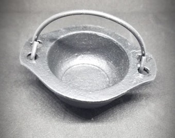 May include: A small black cast iron cauldron with a handle. The cauldron is about 4 inches in diameter and 2 inches tall.