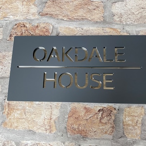 May include: Black metal house sign with the words "Oakdale House" cut out in a white font.