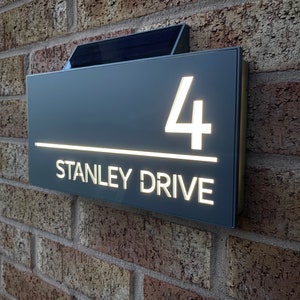 May include: A black and white illuminated house number sign with the number 4 and the text "STANLEY DRIVE" on a brick wall.