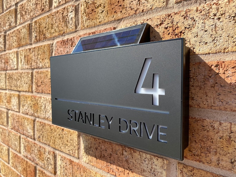 May include: A black solar-powered house number sign with the number 4 and the street name STANLEY DRIVE illuminated in white.