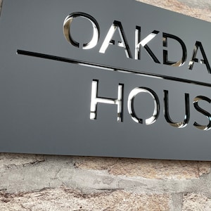 May include: A black metal sign with the words "OAKDALE HOUSE" cut out in a silver reflective material.