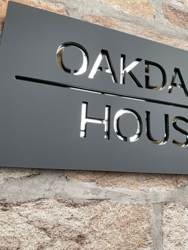 May include: A black metal sign with the words "OAKDALE HOUSE" cut out in a silver reflective material.