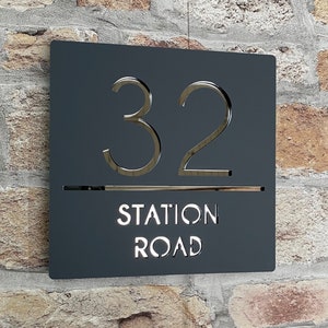 Puede incluir: Un letrero de n&uacute;mero de casa de metal negro con letras blancas. El n&uacute;mero 32 se muestra en una fuente grande, seguido del nombre de la calle "Station Road".