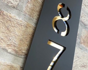May include: Black house number sign with gold numbers 87 cut out. The sign is mounted on a brick wall.