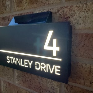 May include: A black house number sign with white illuminated numbers and text. The sign reads "4 STANLEY DRIVE".