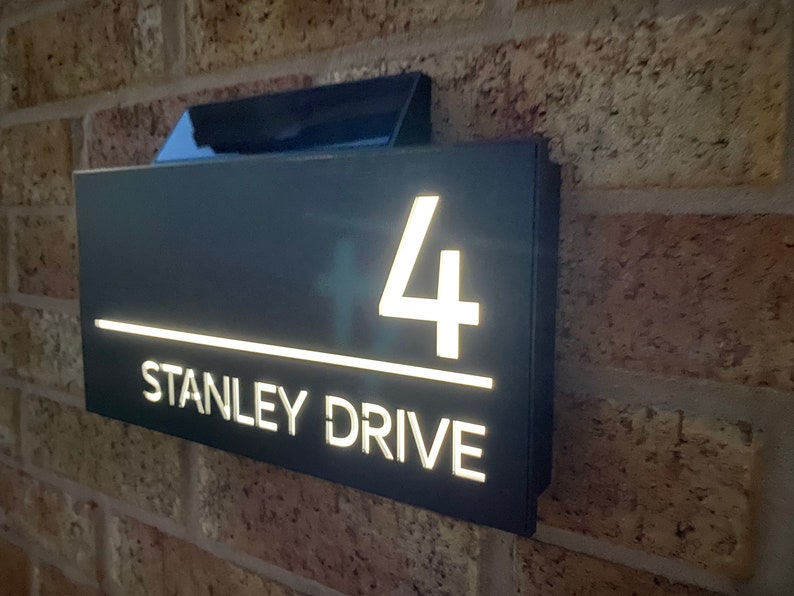 May include: A black house number sign with white illuminated numbers and text. The sign reads "4 STANLEY DRIVE".