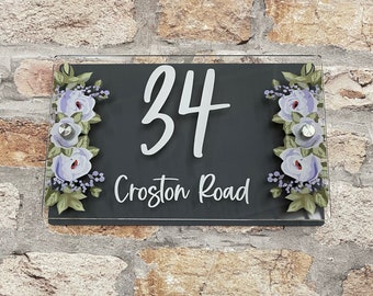 May include: A black and white house number sign with the number 34 and the street name Croston Road. The sign is decorated with a floral design in shades of purple and green.