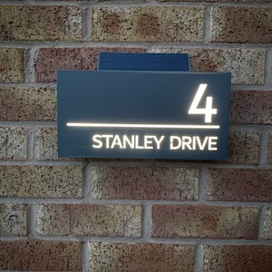 May include: A gray house number sign with white illuminated lettering. The sign reads "4 STANLEY DRIVE".