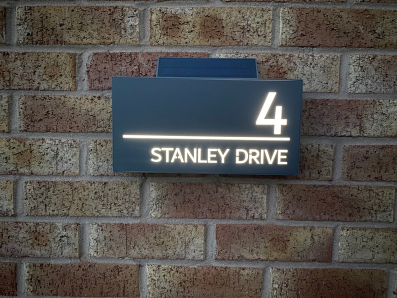 May include: A gray house number sign with white illuminated lettering. The sign reads "4 STANLEY DRIVE".
