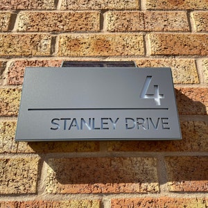 May include: A gray metal house number sign with the number "4" and the text "STANLEY DRIVE" in white lettering.