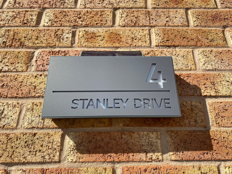 May include: A gray metal house number sign with the number "4" and the text "STANLEY DRIVE" in white lettering.