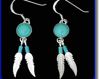 May include: A pair of silver earrings with turquoise-colored circular stones, small blue beads, and feather-shaped pendants. The earrings have a hook closure and are displayed against a dark blue background.