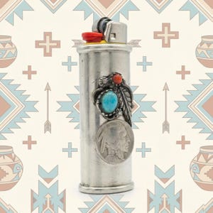 May include: A silver lighter with a red button and a decorative turquoise stone, coral, and feather design. A silver coin with a profile is also attached. The lighter has a Native American theme.