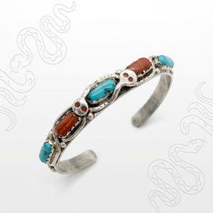 May include: A silver cuff bracelet featuring alternating turquoise and reddish-brown stones. The bracelet has a decorative design with small skull-like accents. The open-ended design allows for easy wear. This piece is a unique accessory.