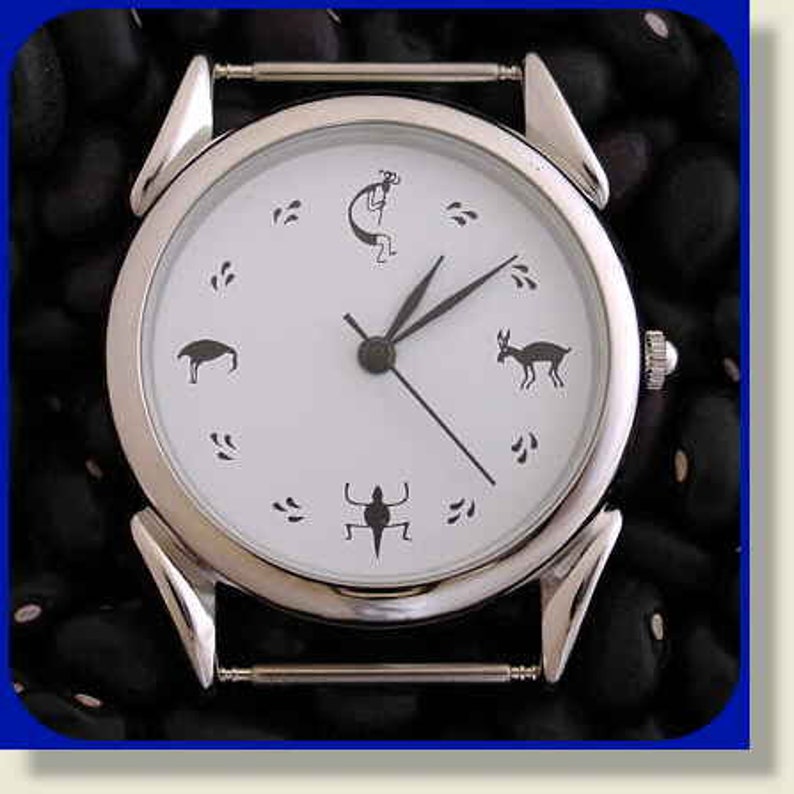 May include: A silver wristwatch with a white face and black markings. The watch face features a stylized design with animal and human figures.