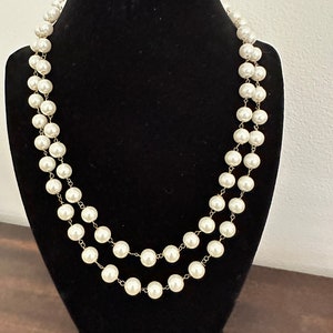 May include: A double strand pearl necklace with gold-toned metal clasps. The pearls are white and round.