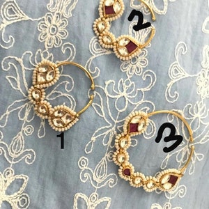 May include: Two gold nose rings with pearl and red gemstone accents. The rings are numbered 1 and 2.