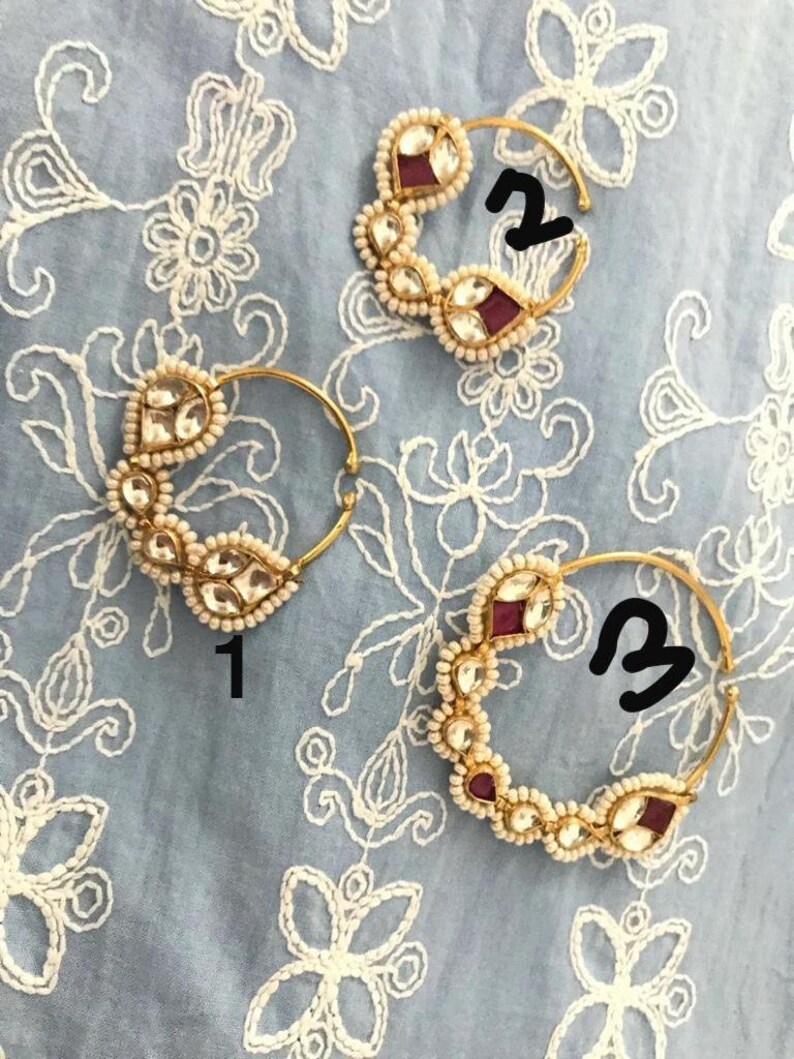 May include: Two gold nose rings with pearl and red gemstone accents. The rings are numbered 1 and 2.