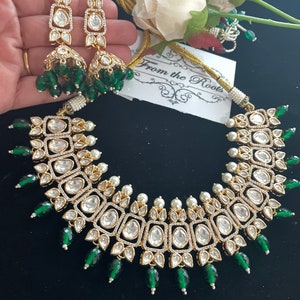 May include: A gold and white necklace with green accents. The necklace features a square design with multiple layers of stones. The necklace is paired with matching earrings.