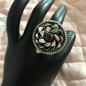 May include: A silver ring with a large flower design and a pink gemstone in the center.