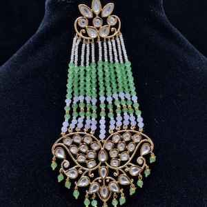May include: A gold-toned hair ornament with a floral design and a long beaded tassel. The tassel is made of white, green, and light pink beads.