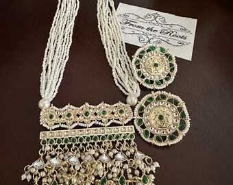 May include: A multi-strand pearl necklace with a gold and green pendant featuring intricate designs and a tassel of pearls and green stones. The pendant has a rectangular shape with a smaller rectangular section at the top. The necklace is accompanied by a pair of matching earrings.
