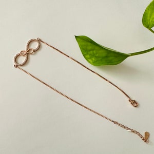 May include: A rose gold infinity necklace with a clear crystal infinity symbol. The necklace has a box chain and a lobster clasp.