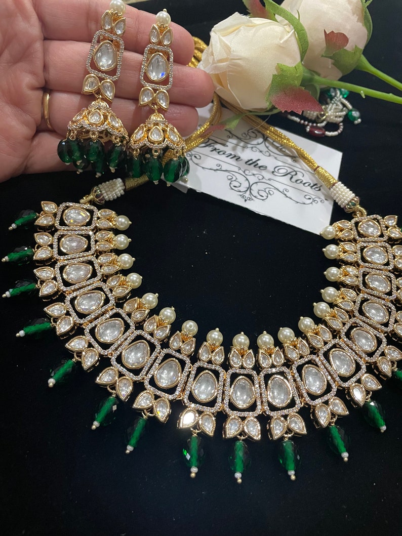 May include: A gold necklace with a square design and green and white beads. The necklace is accented with pearls and has a matching pair of earrings.