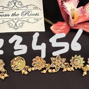 May include: Eight gold nose rings with different designs and pearl accents. The rings are numbered 1 through 8. From the Roots.