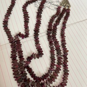 May include: A multi-strand necklace made of dark purple faceted beads. The necklace has a silver clasp with a decorative design.