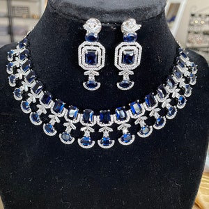 May include: A silver necklace and earrings set with blue and clear cubic zirconia stones. The necklace features a layered design with multiple rows of stones.
