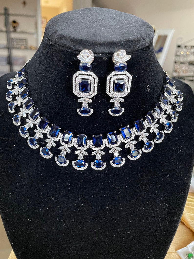 May include: A silver necklace and earrings set with blue and clear cubic zirconia stones. The necklace features a layered design with multiple rows of stones.