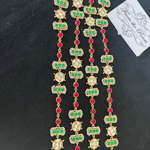 May include: Three gold chains with green and red stones, and white pearls. The chains are on a black background. The text "From the Roots" is visible on a white card.