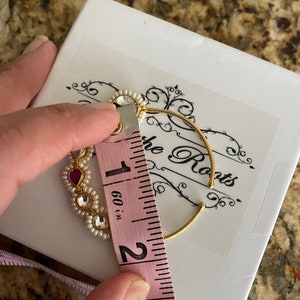 May include: A gold nose ring with white pearls and pink stones, measuring 1.6 inches in diameter. The ring is on a white box with the words "The Roots" printed on it.