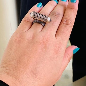 May include: A silver ring with a detailed, openwork design. The ring is worn on the index finger of a hand with turquoise nail polish.
