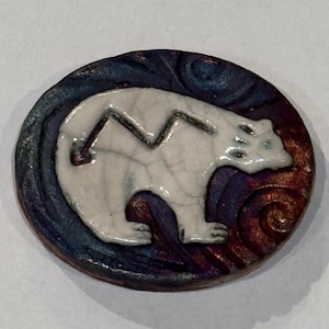 May include: A ceramic polar bear design on a round, decorative piece. The bear is white with a black zig-zag design on its back. The background features swirling patterns in shades of blue, purple, and brown.