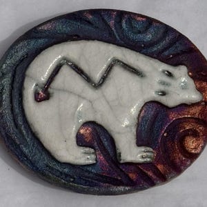 May include: A round ceramic piece featuring a white polar bear design. The bear is centered on a background with swirling patterns in shades of blue, purple, and bronze. The edges of the piece are dark blue.