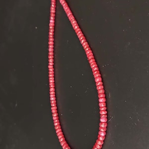 May include: A strand of red gemstone beads, likely ruby, strung on a thin cord. The beads are faceted and have a slight shimmer.