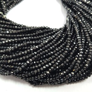 May include: A close-up of a collection of black faceted beads. The beads are strung together, creating a dense, textured appearance. The beads have a shiny, reflective surface, and are likely used for jewelry making.