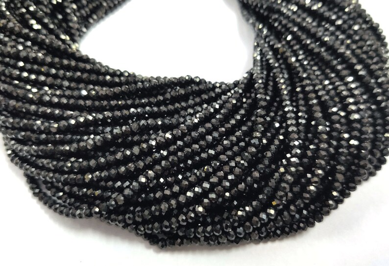 May include: A close-up of a collection of black faceted beads. The beads are strung together, creating a dense, textured appearance. The beads have a shiny, reflective surface, and are likely used for jewelry making.