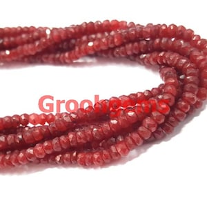 Peut inclure: Un brin de perles de pierres précieuses facettées rouges. Les perles sont petites et ont une taille facettées, ou en forme de diamant. Les perles sont enfilées sur un fil transparent.